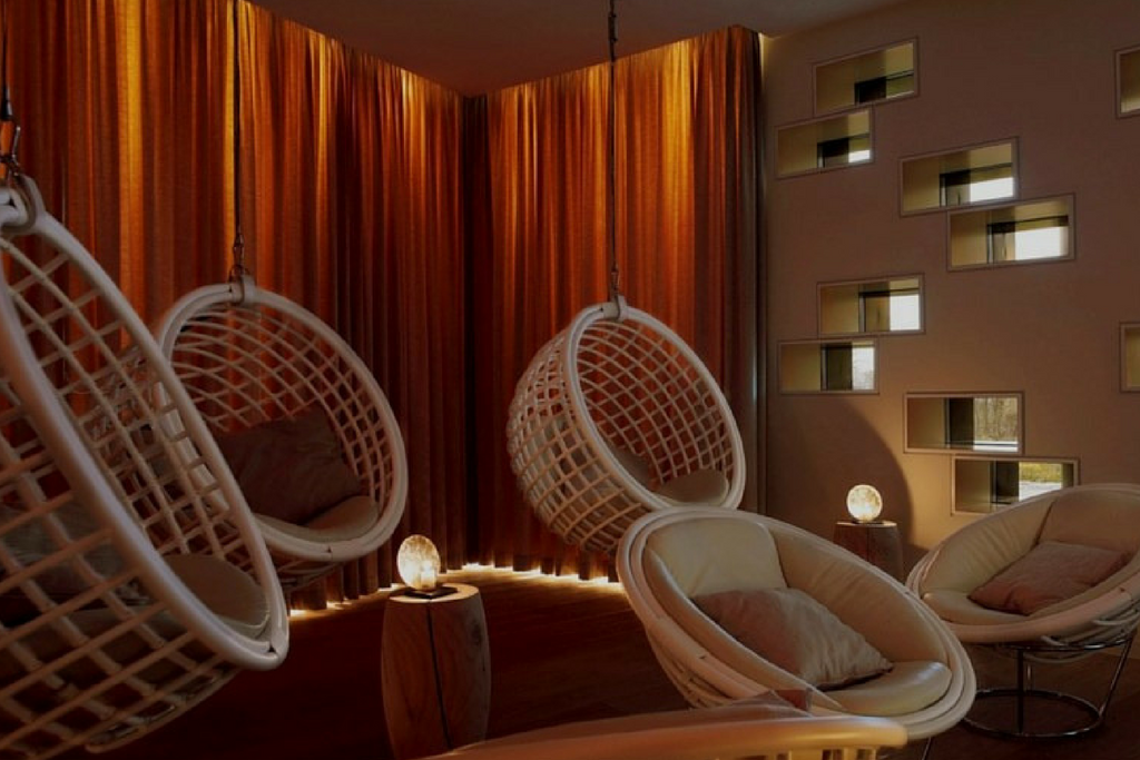 A dark room lit up by wall inserted lights and surrounded by multiple white round chairs