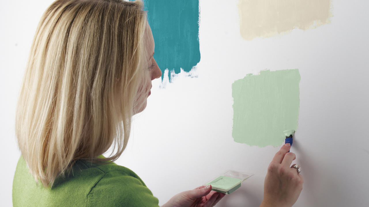 how to paint a room a woman testing paint on a white wall