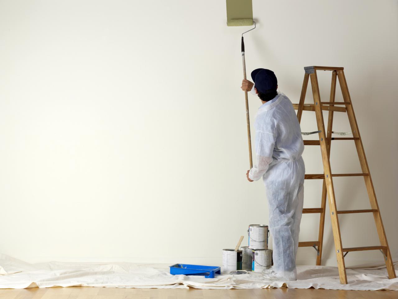 man painting a white room beige with a roller extension poll