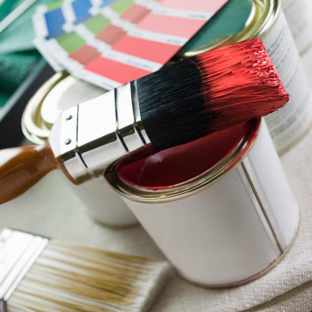 a paint brush that has been dipped in red paint sits on top of a paint tin