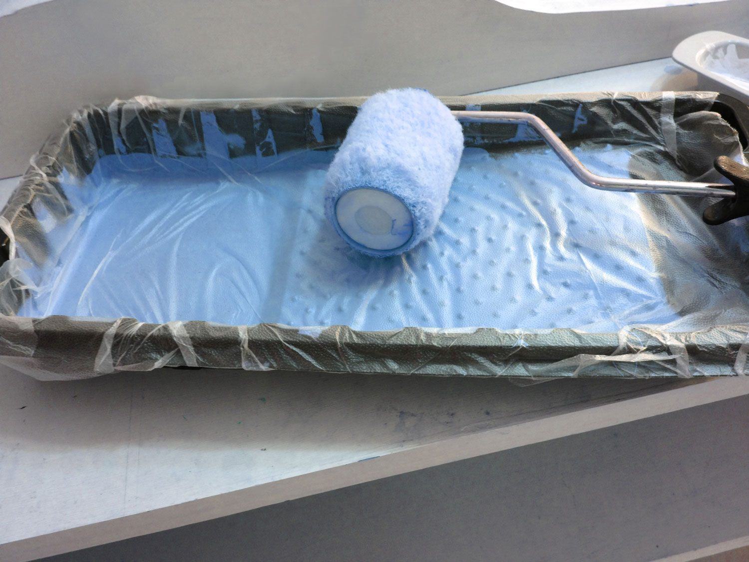 plastic bag sits over a used paint tray with a used roller on top for protection