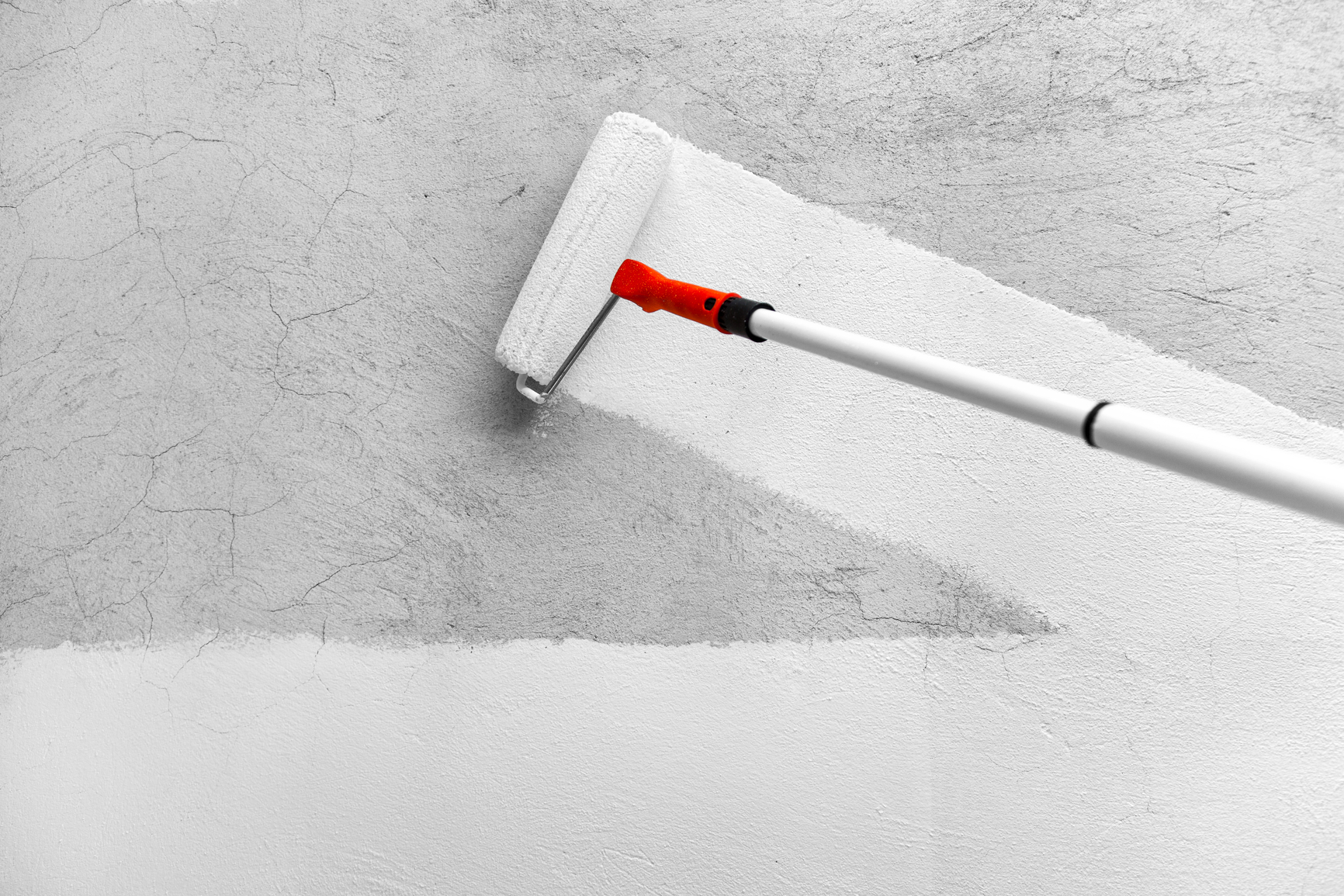 a paint roller paints a rough wall in white latex paint
