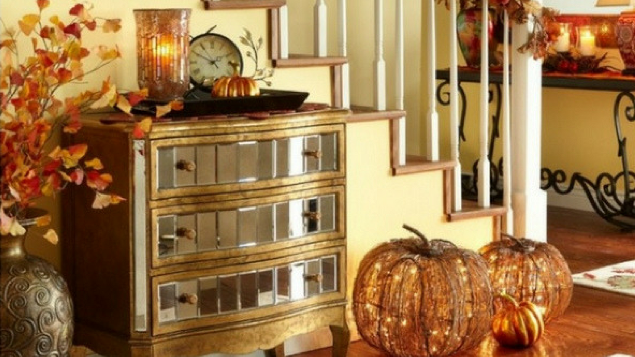 autumn decorations adorn a stairways with orange pumpkin lights, vase with leaves and a glass cabinet topped with candles