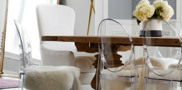 glamorous style faux fur draped over clear chairs around a wooden table with flowers on top near a large mirror
