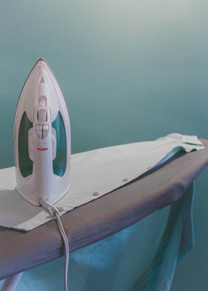 an iron is sat on an ironing board with a white shirt laid out in front