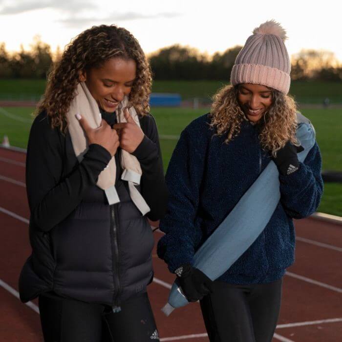 two women walking around a running track with a hot water bottle around their necks