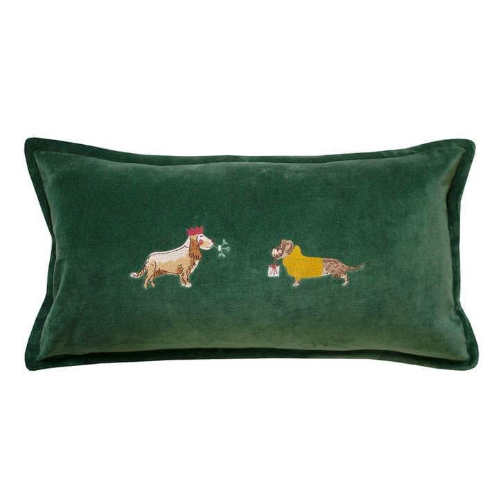 a green velvet cushion with dog figures with festive wear on a cut out white background