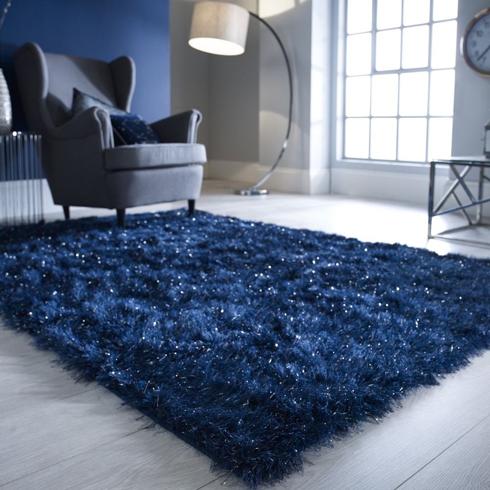 the dazzle midnight blue shaggy rug with shimmer thread is set on a floor in a living room space 