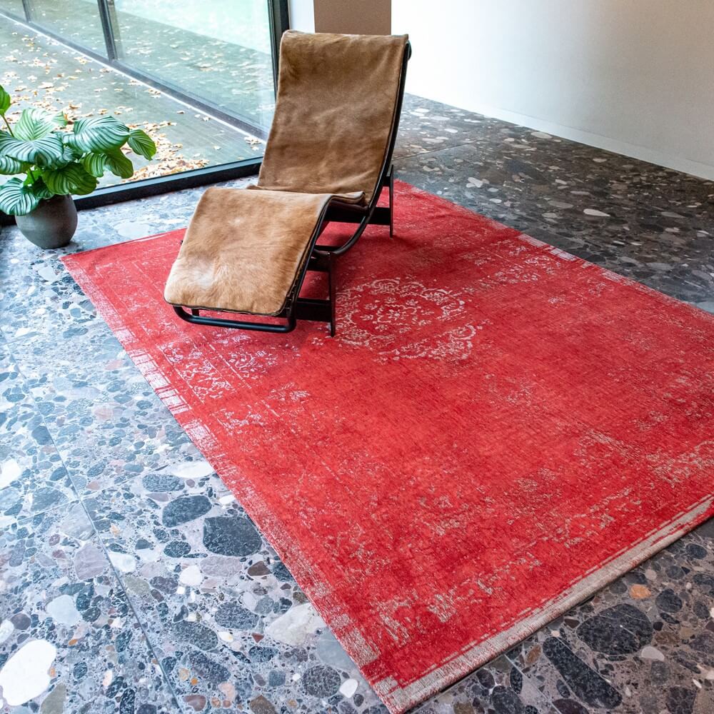 a louis de poortere red rug set on a tiled floor with a chair set on top