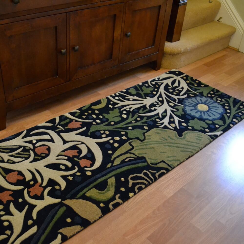 a Morris & co runner with seaweed patterns on a dark background is laid on a wooden floor in a hallway