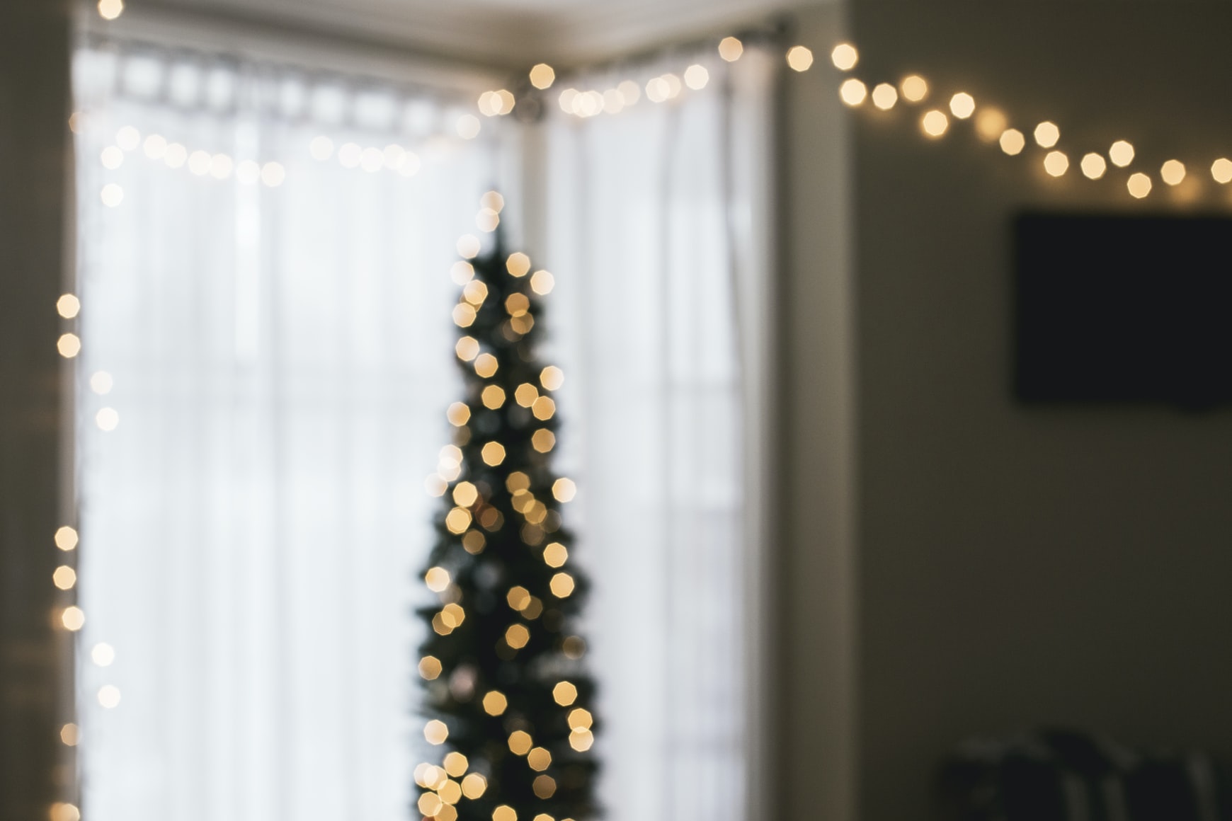 a room with fairy lights strung around as well as a narrow christmas tree set up with fairy lights