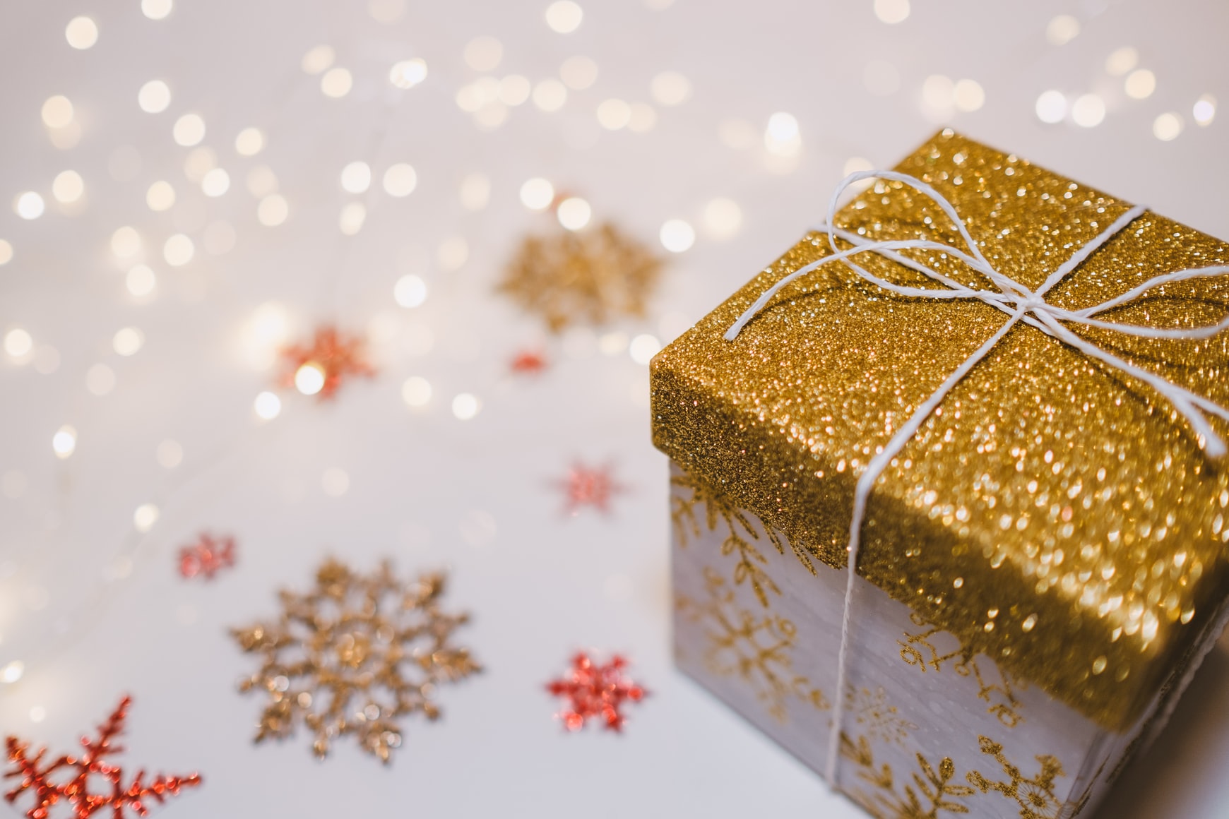 a christmas present box with a gold glittery lid is set on a surface with lights and gold snowflakes