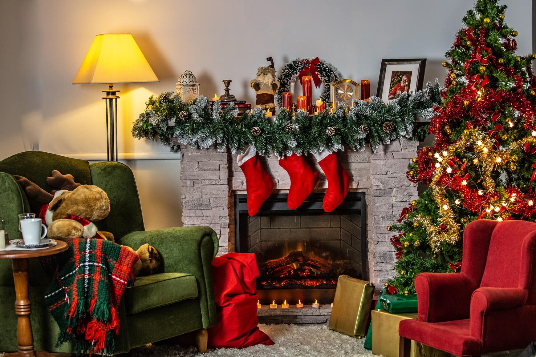 a living room christmas interior full of reds and greens with stockings on a fireplace and a christmas tree