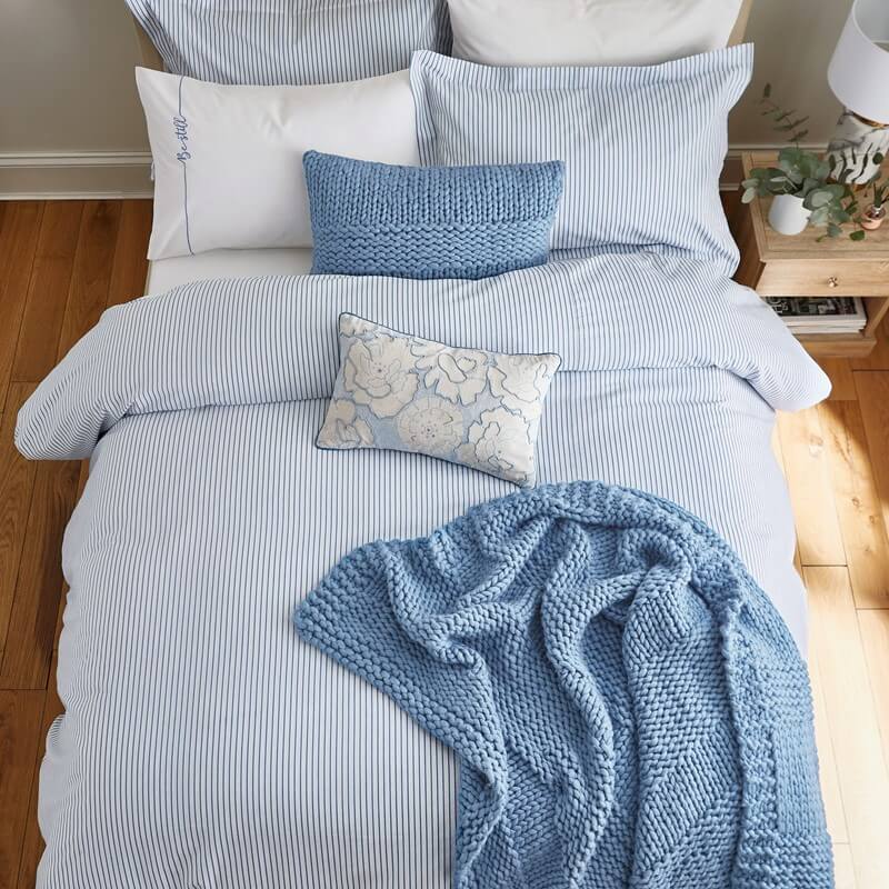 a chunky wool blanket thrown on a bed with blue bedding in a wooden and modern bedroom