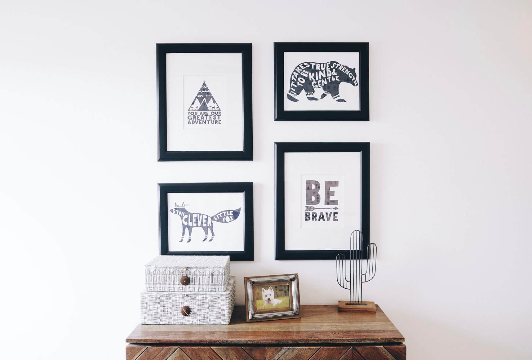 a wall has four images with black and white artwork on a white wall above a wooden cabinet
