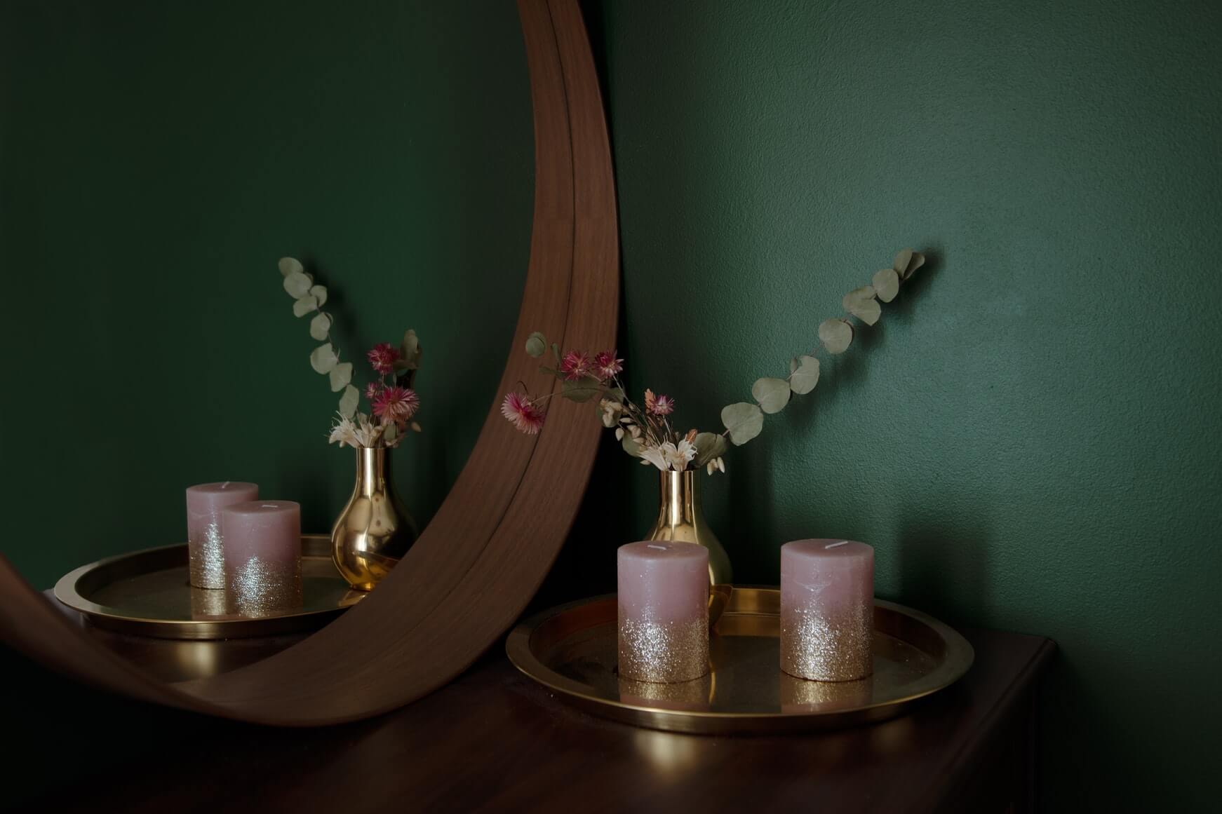 a green wall with a mirror and cabinet set against it with greenery and a candle