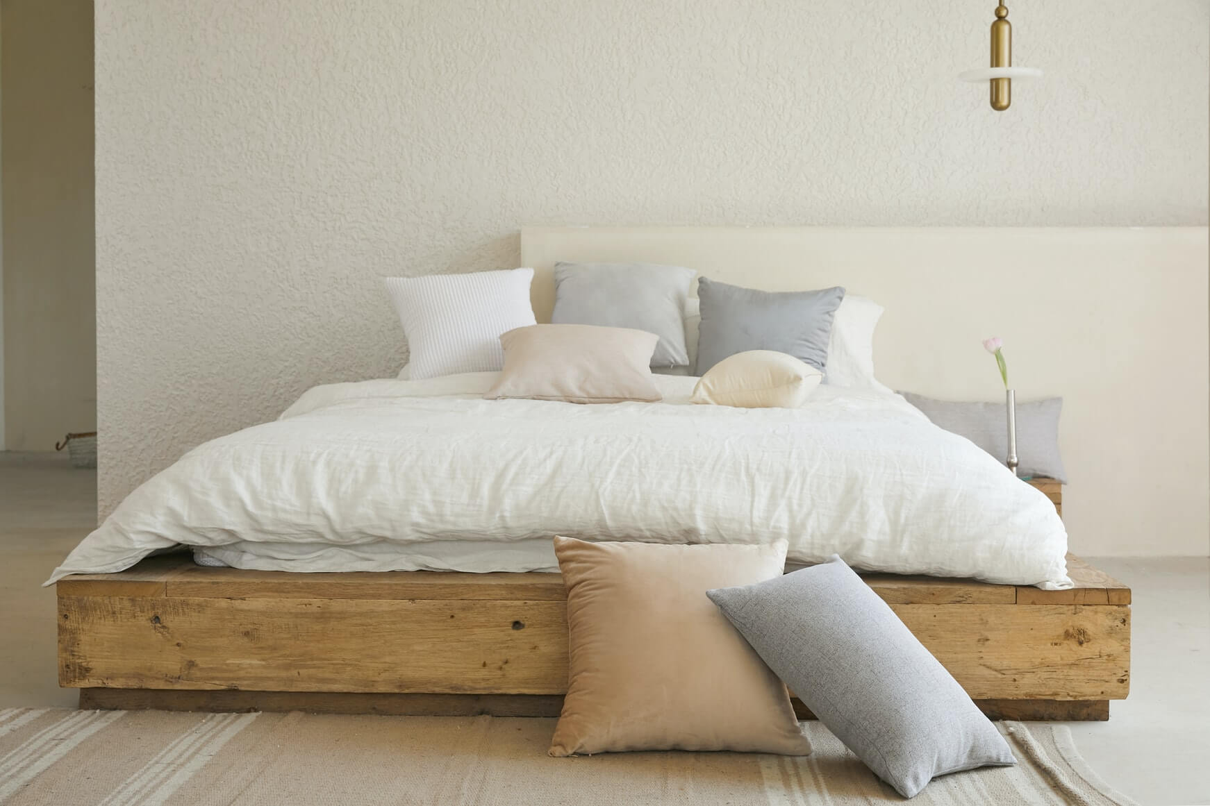 low bed in a bedroom with white bedding and pastel colour cushions