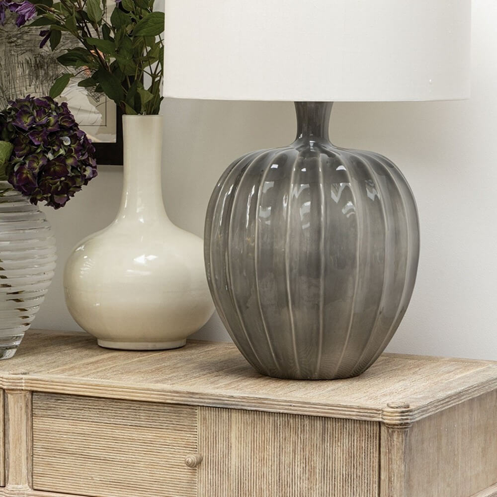 a grey ceramic lamp sat on a wooden sideboard