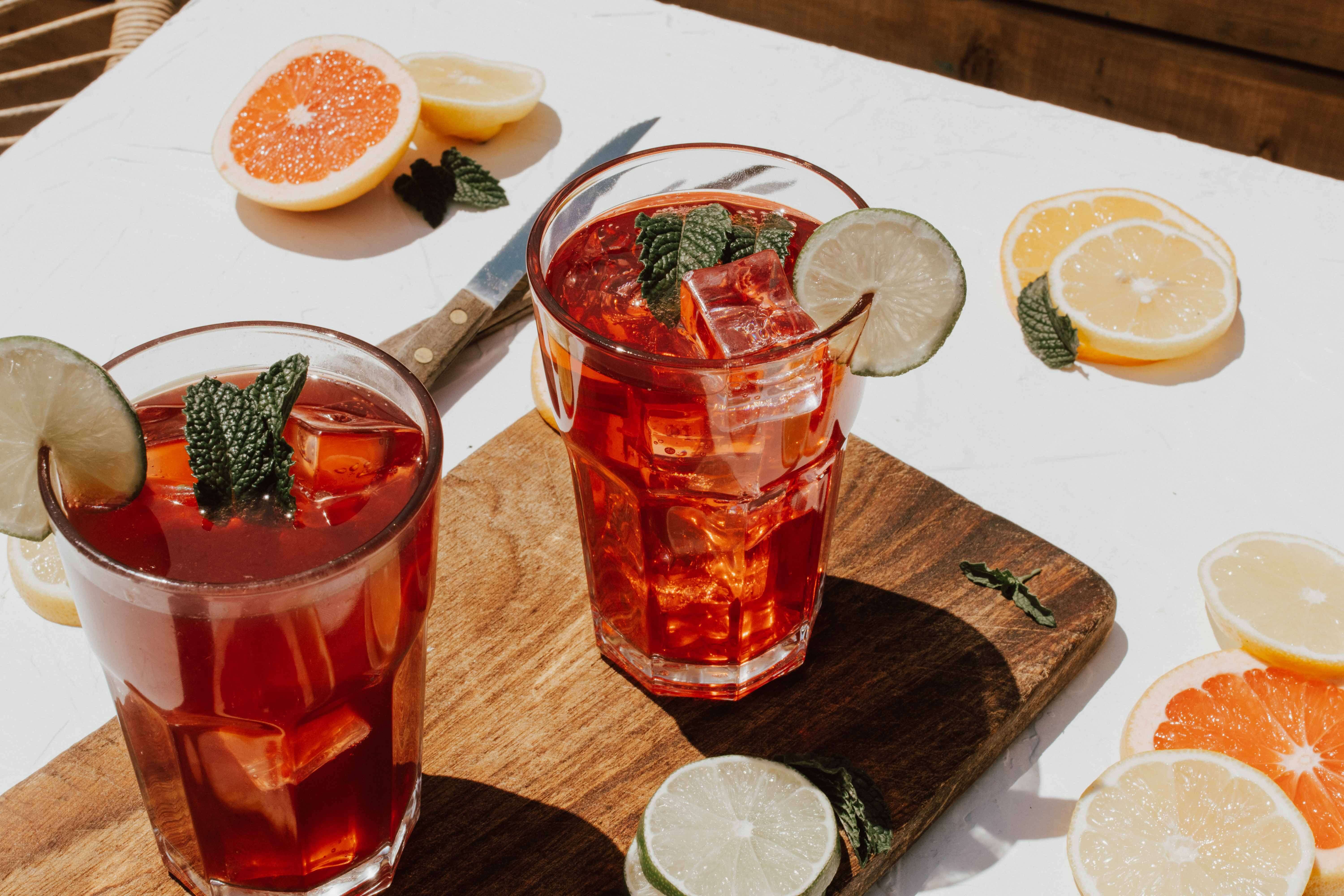 host a summer bbq with cocktails like these two red glasses of pimms sat on a table in the sun surrounded by fruit